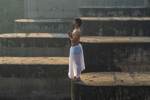 The young Indian priest praying to the sun early in the morning while wearing a dhoti.