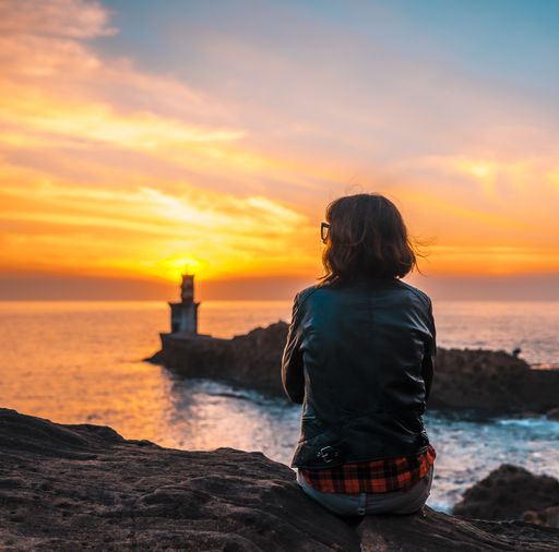 A young woman near the lighthouse during a beautiful orange sunset in the Pasajes San Juan, Gipuzkoa, Spain