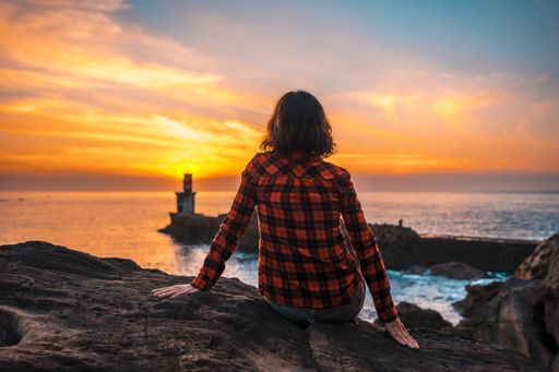 A young woman near the lighthouse during a beautiful orange sunset in the Pasajes San Juan, Gipuzkoa, Spain