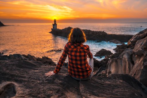 A young woman near the lighthouse during a beautiful orange sunset in the Pasajes San Juan, Gipuzkoa, Spain
