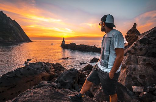 A young man near the lighthouse during a beautiful orange sunset in the Pasajes San Juan, Gipuzkoa, Spain