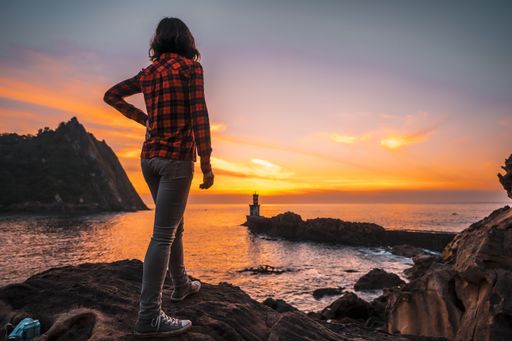 A young woman near the lighthouse during a beautiful orange sunset in the Pasajes San Juan, Gipuzkoa, Spain