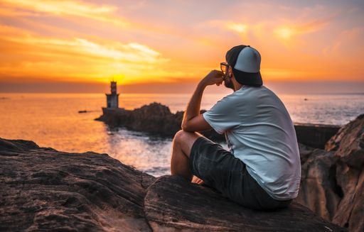 A young man near the lighthouse during a beautiful orange sunset in the Pasajes San Juan, Gipuzkoa, Spain