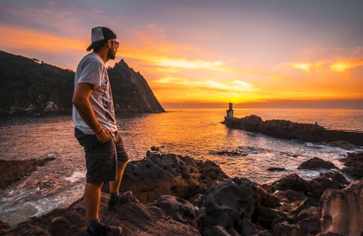 A young man near the lighthouse during a beautiful orange sunset in the Pasajes San Juan, Gipuzkoa, Spain