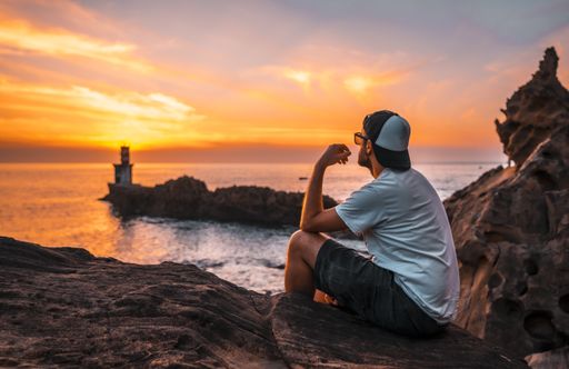 A young man near the lighthouse during a beautiful orange sunset in the Pasajes San Juan, Gipuzkoa, Spain