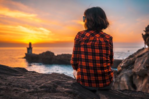 A young woman near the lighthouse during a beautiful orange sunset in the Pasajes San Juan, Gipuzkoa, Spain