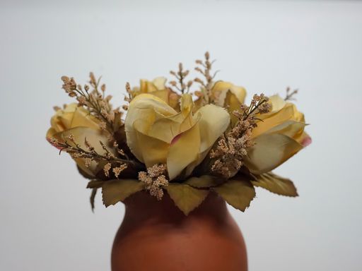 The artificial yellow roses in a clay vase against a white background