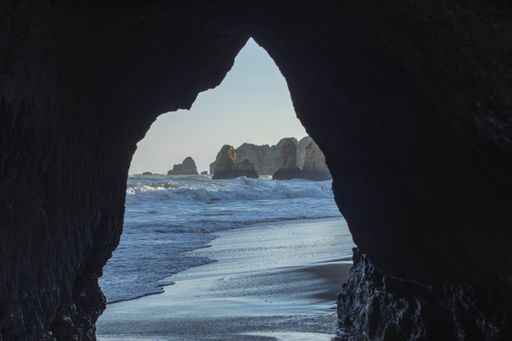 A mesmerizing view of the cliffs over the splashing sea water from the arched stone at the beach