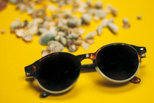 A closeup shot of sunglasses with seashells on yellow background-perfect for wallpaper