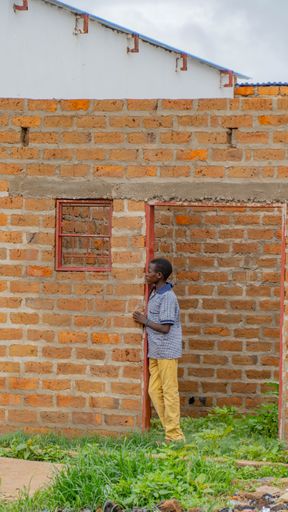 A black kid standing under an abandoned brick building entrance