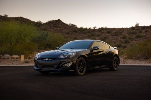 A black Genesis car is parked on the side of a street, facing away from the viewer