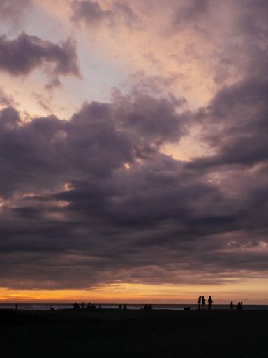 A vertical shot of the cloudy sunset sky over the beach with people seen in the distance