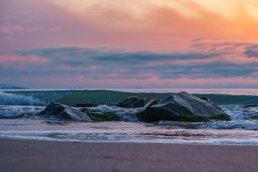 A lovely view of a beach at sunset with high tides crashing against sharp rocks under a cloudy sky