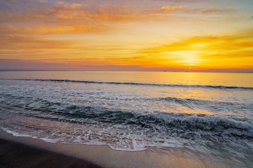 A gorgeous view of a sunset at sea with low tides at the shore under a bright orange cloudy sky