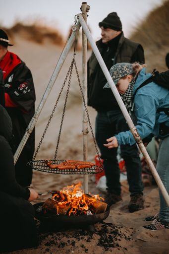 A vertical shot of people grilling sausages over a bonfire