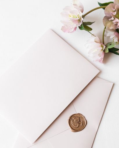 A vertical shot of two pink envelopes for invitations on a white background, with pink flowers beside, copy space