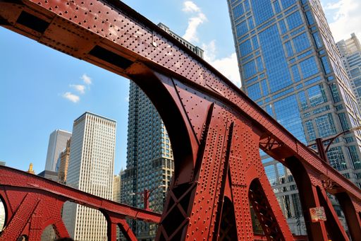 A low angle shot of a red iron bridge and high-rise buildings Chicago