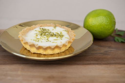A closeup of a key lime tartlet on a plate and a key lime fruit on a wooden board