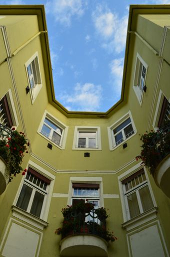 A vertical low angle shot of yellow residential building under blue sky and white clouds