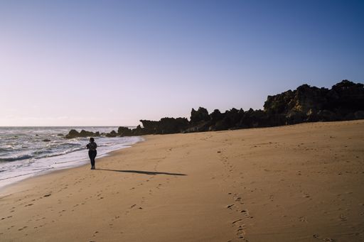 A person standing on the beautiful sandy beach by the ocean and the huge rocks on a sunny day