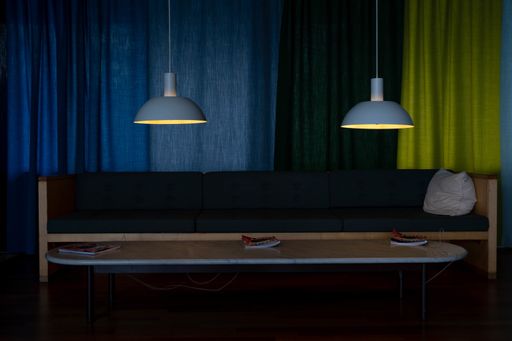 A beautiful dark blue sofa by a wooden table in front of colorful curtains and two pedant lamps