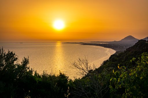 An aerial view of the calm Ionian sea and the Corfu Island gleaming under the sunset on the coast
