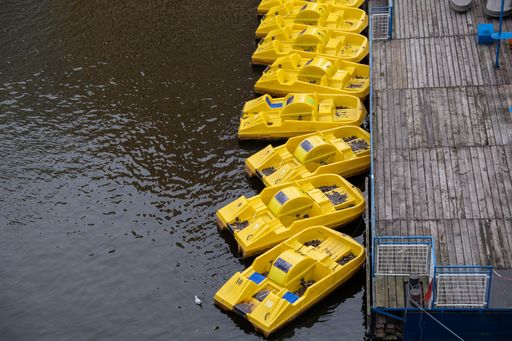 A high angle shot of the yellow pedal boats tired to the wooden pier on the calm surface of the water