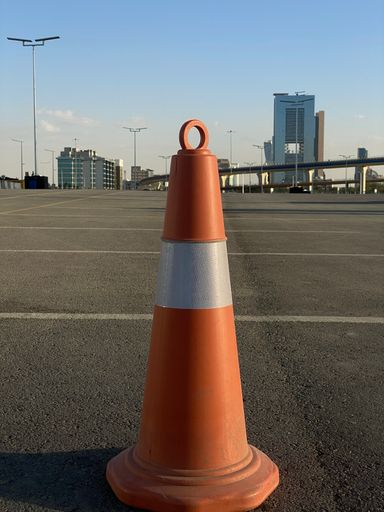 A vertical shot of an orange traffic cone on an asphalt ground in sunny weather