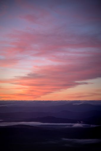 A vertical shot of a snowy hills against a colorful cloudy sky during a sunset
