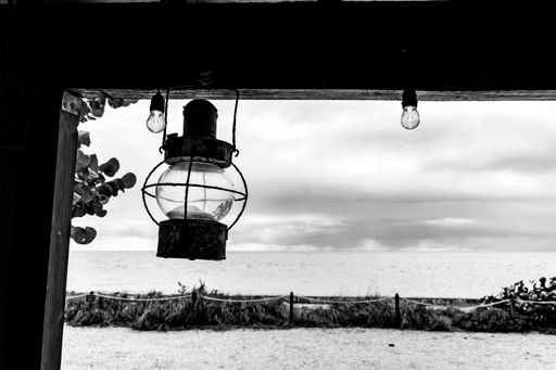 A closeup shot of an old hanging lantern on a snady beach background on a grayscale