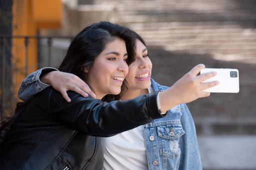 Two beautiful Hispanic girls taking a selfie with a smartphone outdoors