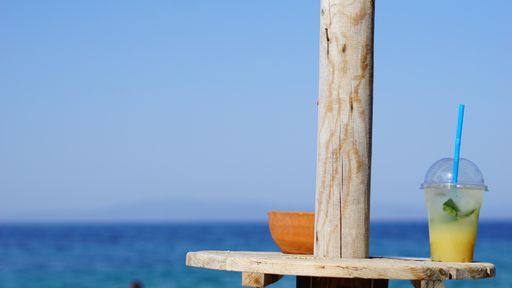 A closeup shot of a cocktail in a plastic cup with the sea on the background