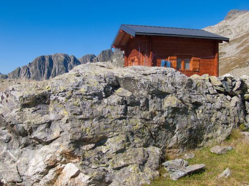 A low angle shot of a small red house near cliffs in Lac de la Combe, Haute Savoie, France