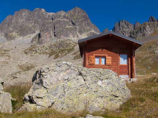 A low angle shot of a small red house near cliffs in Lac de la Combe, Haute Savoie, France