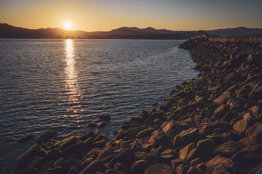 The golden sunset slowly disappearing behind the mountains and shining the sea surrounded with rocks