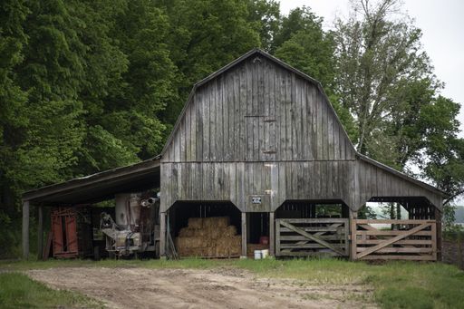 An eye-level shot of a wooden barn standing next to green trees with a haystack inside