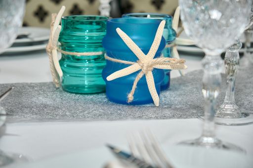 A close up shot of candles in blue colored glass jars in marine style