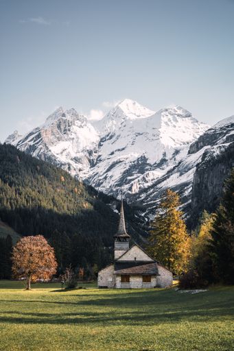 Typical Swiss mountain church in autumn in Kandersteg, Bern, Switzerland, with golden trees and snow capped mountains