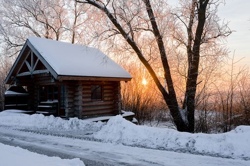 A winter landscape of a wooden house along the road during sunset
