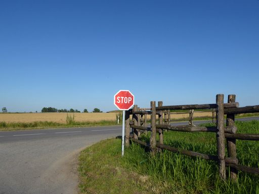 A red stop sign at the end of a country road at an intersection