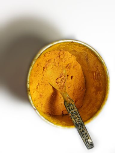 A high angle shot of turmeric powder in a bowl with a spoon in it on the table