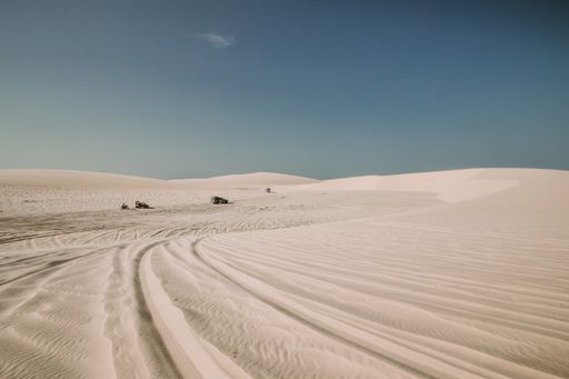 A landscape shot of a desert with tire marks on the sand and motor vehicles in the distance