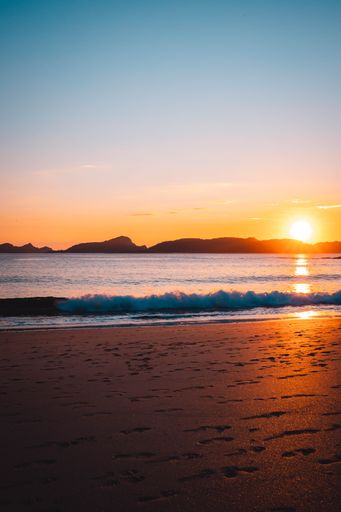 A vertical sunset shot over a sandy beach surrounded by mountains