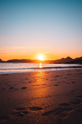 A vertical sunset shot over a sandy beach surrounded by mountains