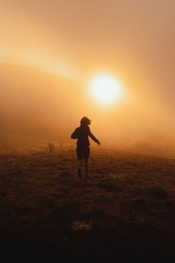 A silhouette of a person running on a hill towards the sunset