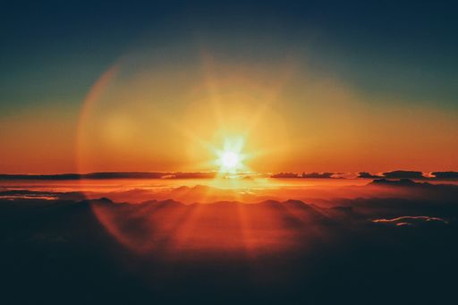 A horizontal shot of a sunset from a mountain cliff with the sun visible in the distance