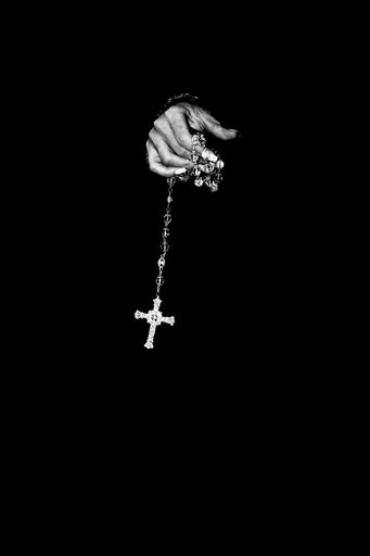 A vertical shot of a person's hand holding a cross on a chain in a pitch-black background