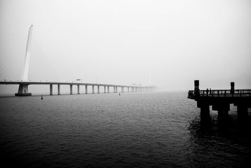 A grayscale shot of a long bridge over the lake