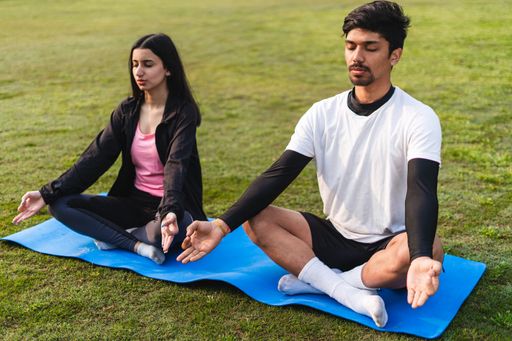 A young couple doing yoga and meditating in the park - concept of healthy lifestyle