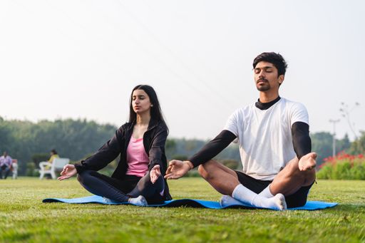 A young couple doing yoga and meditating in the park - concept of healthy lifestyle